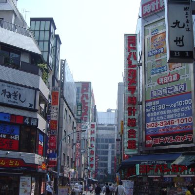 A busy Tokyo street lined with stacked billboards and illuminated advertising signs on the building fronts